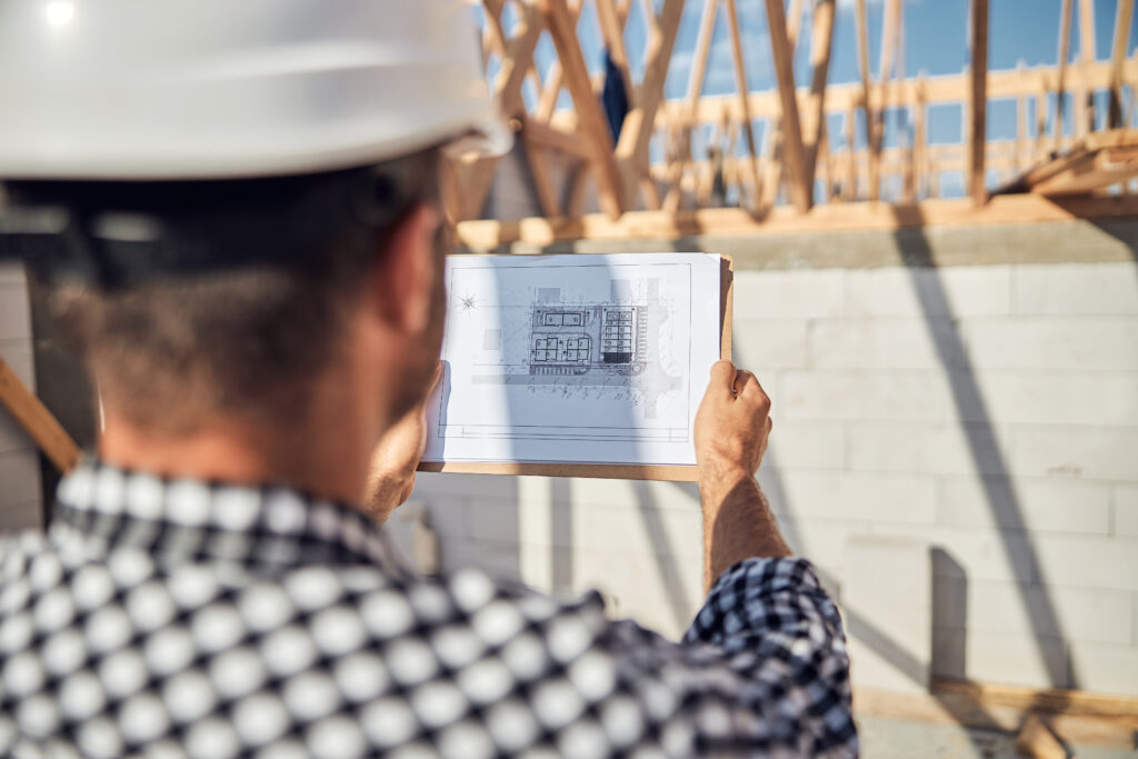 Focused man in a hard hat looking closely at a sheet of paper with plan of a building | footing cost calculator